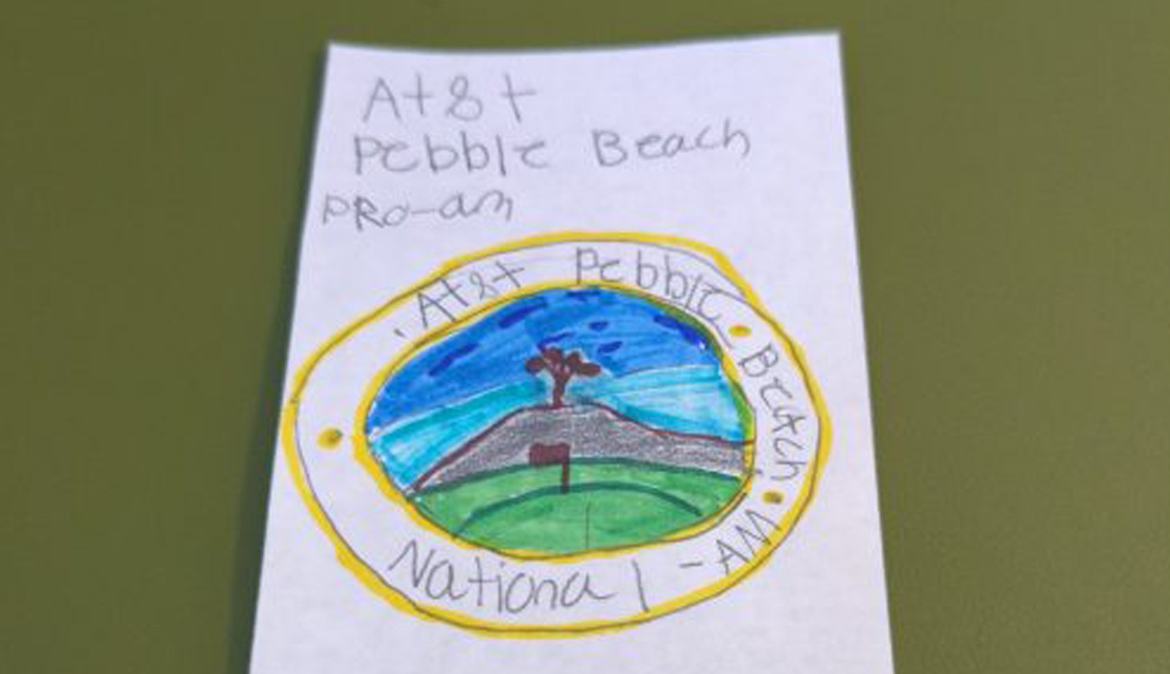 A child's drawing resembling a tournament logo, featuring a tree on a hill with a flagstick, surrounded by a yellow ring with handwritten text: