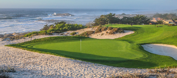 A historical-style photo of a golf green nestled in sand dunes next to the ocean. Waves crash onto the rocks and beach in the background.