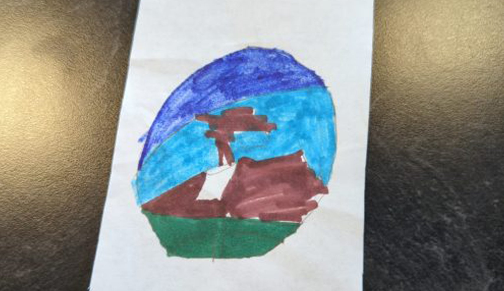 A child's drawing inside an oval frame, crudely colored blue and green, featuring a dark brown tree and rocky landscape with a person and a flag on the course.