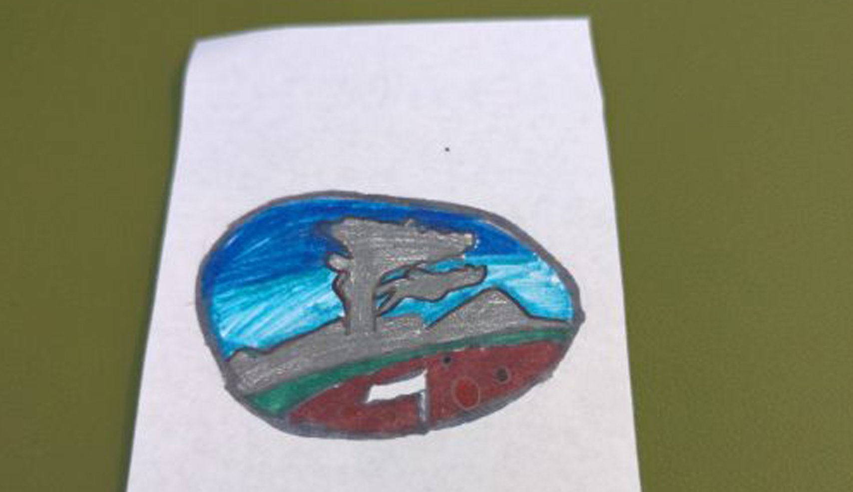 A child's drawing inside an oval, showing a gray silhouette of the Lone Cypress tree on a green and red landscape against a blue sky. A golf flag is visible in the red section.