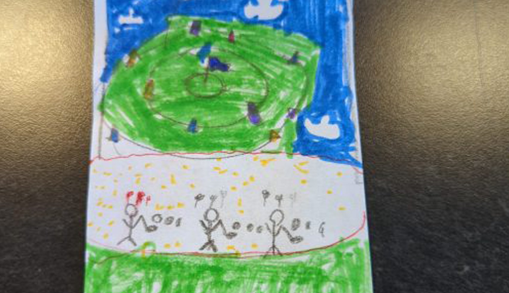 A colorful child's drawing depicting an aerial view of a circular golf green surrounded by blue sky and white clouds, with stick-figure golfers on a sandy area below.