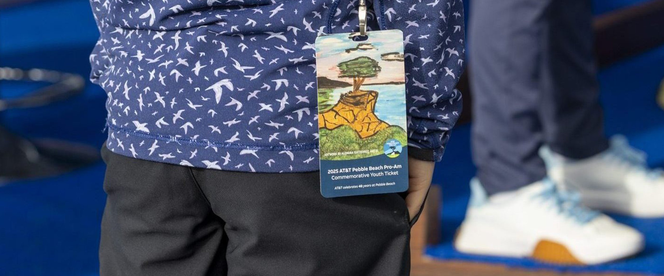 A close-up of an event pass on a lanyard, featuring a child's drawing of a tree on a cliff as the
