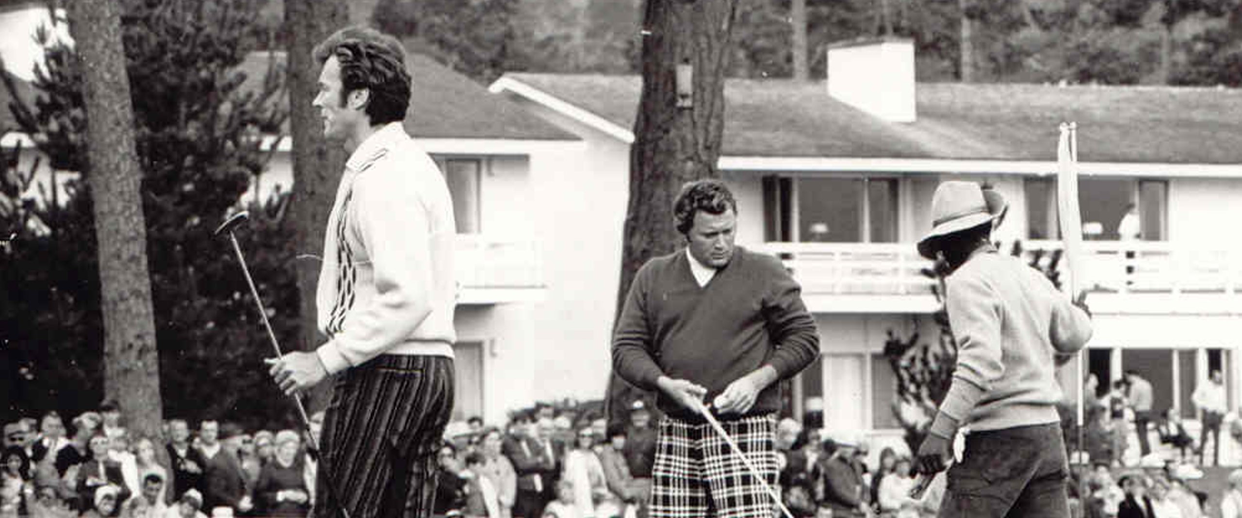 A classic black and white photo from the tournament's history, showing Clint Eastwood (far left) and two other men on the golf course in front of a crowd, all wearing vintage golf attire.