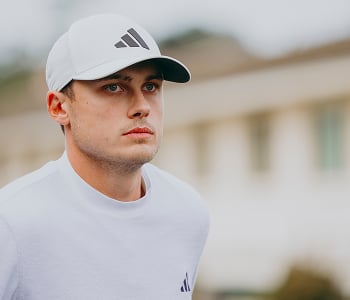A close-up headshot of golfer Ludvig Åberg looking off-camera with a neutral expression, wearing a white t-shirt and a white Adidas cap.